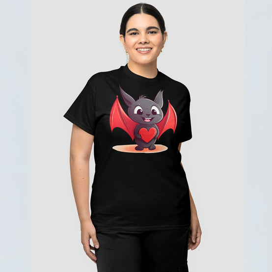 A smiling woman wearing a black t-shirt adorned with a cute cartoon bat character in the center holding a red heart, showcasing a playful and loving design.