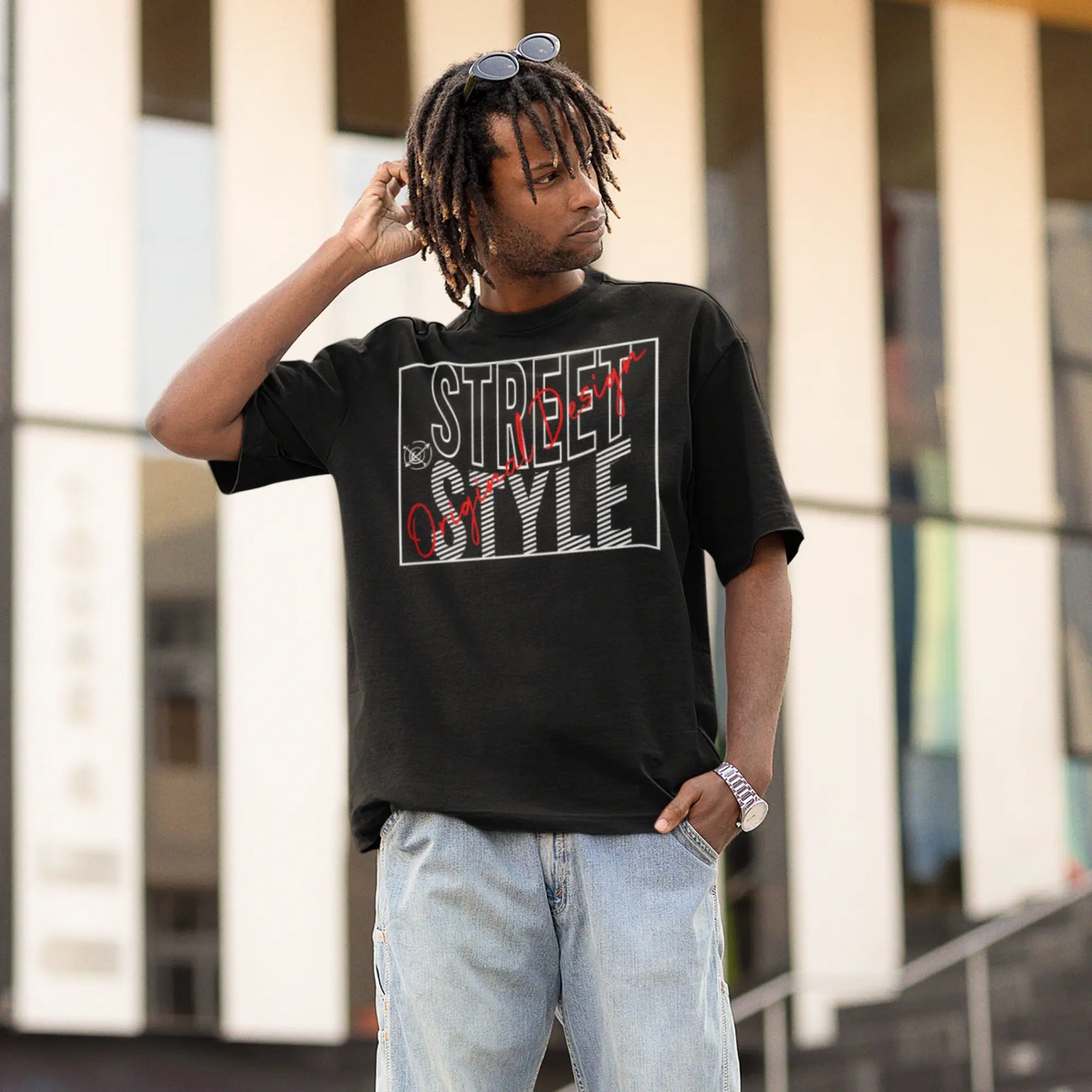 A man with dreadlocks wearing sunglasses atop his head stands casually in an urban setting, donning a black t-shirt with a bold 'STREET STYLE' graphic in stylized white and red fonts, with a small drawing of sunglasses adding to the design's urban aesthetic.