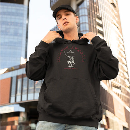 A young man in an urban setting, wearing a cap and holding the hood of his black hoodie which features the 'Beverly Hills Polo Club' logo with a polo player on horseback and the words 'Limited Edition' underneath. The casual yet stylish hoodie contrasts with the modern high-rise buildings in the background.