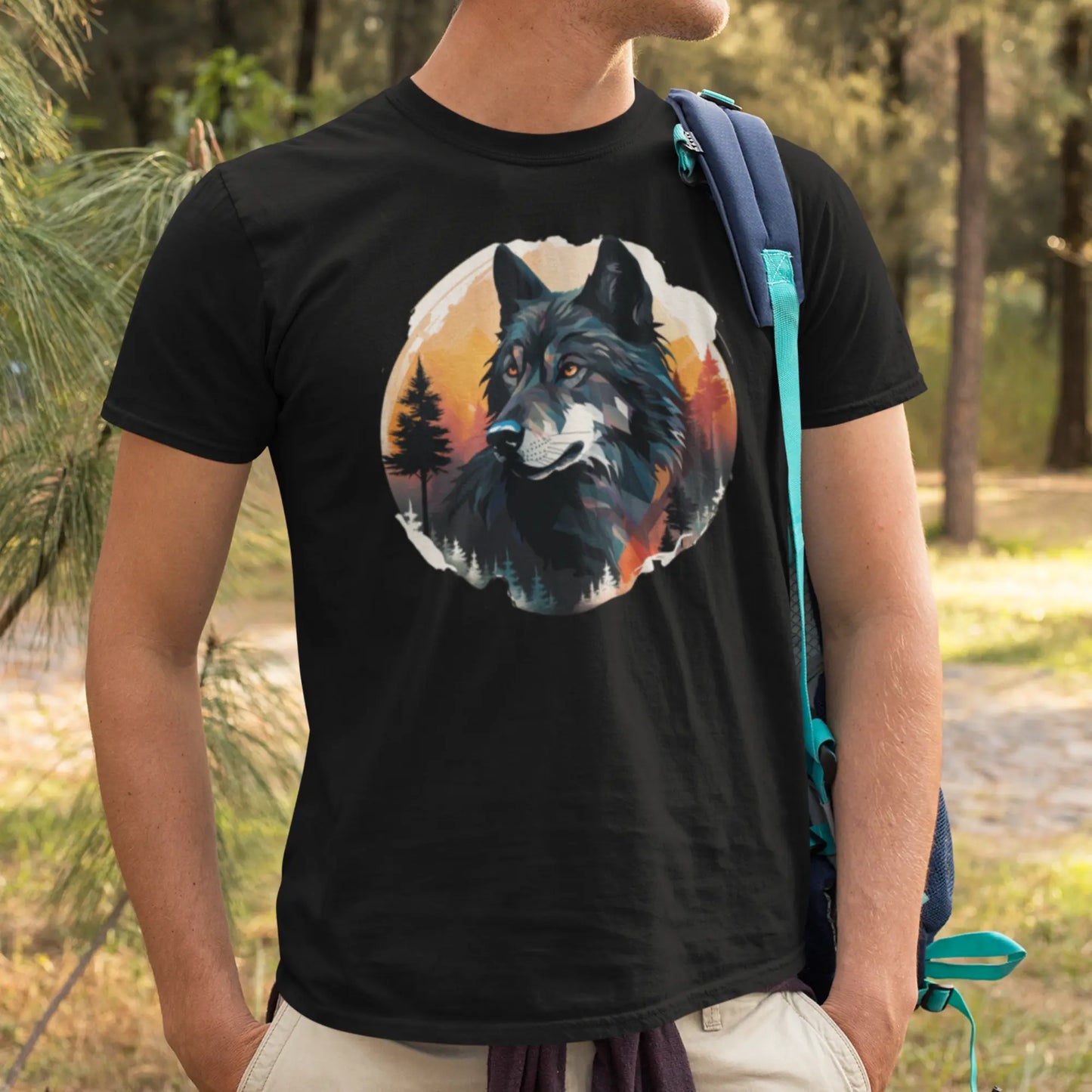 A man with a blue shoulder bag stands in a forested area, wearing a black t-shirt featuring a large, colorful graphic of a wolf's head. The graphic is styled with warm autumnal hues in the background, with the wolf's gaze appearing noble and serene.