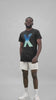  A confident man in a studio posing with a black t-shirt featuring a stylized 'X' with a sea wave print within it.