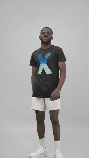  A confident man in a studio posing with a black t-shirt featuring a stylized 'X' with a sea wave print within it.