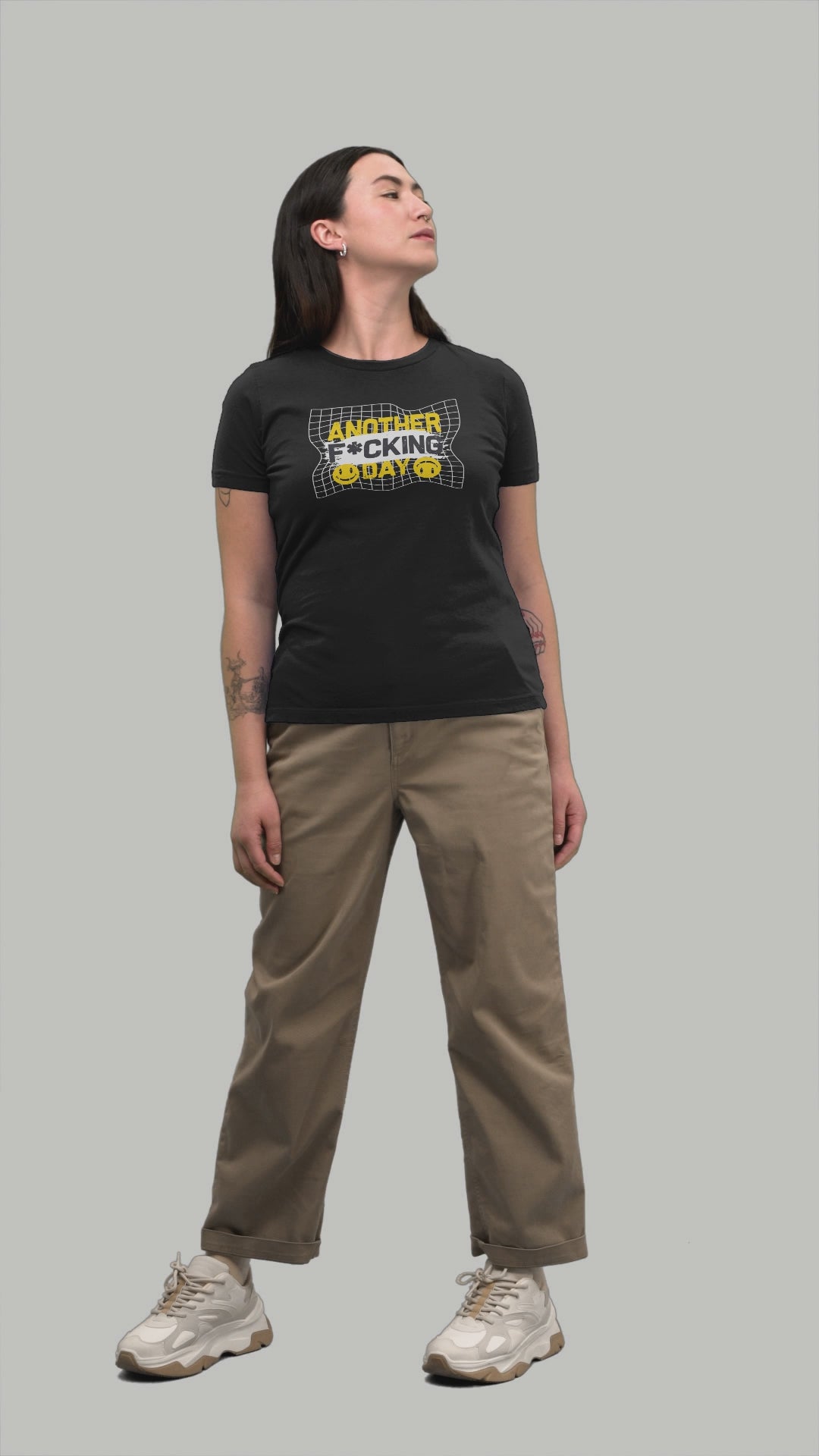 Woman in a black t-shirt with a graphic design featuring bold yellow text 'ANOTHER F*CKING DAY' with a distressed grid background and two smiley faces.